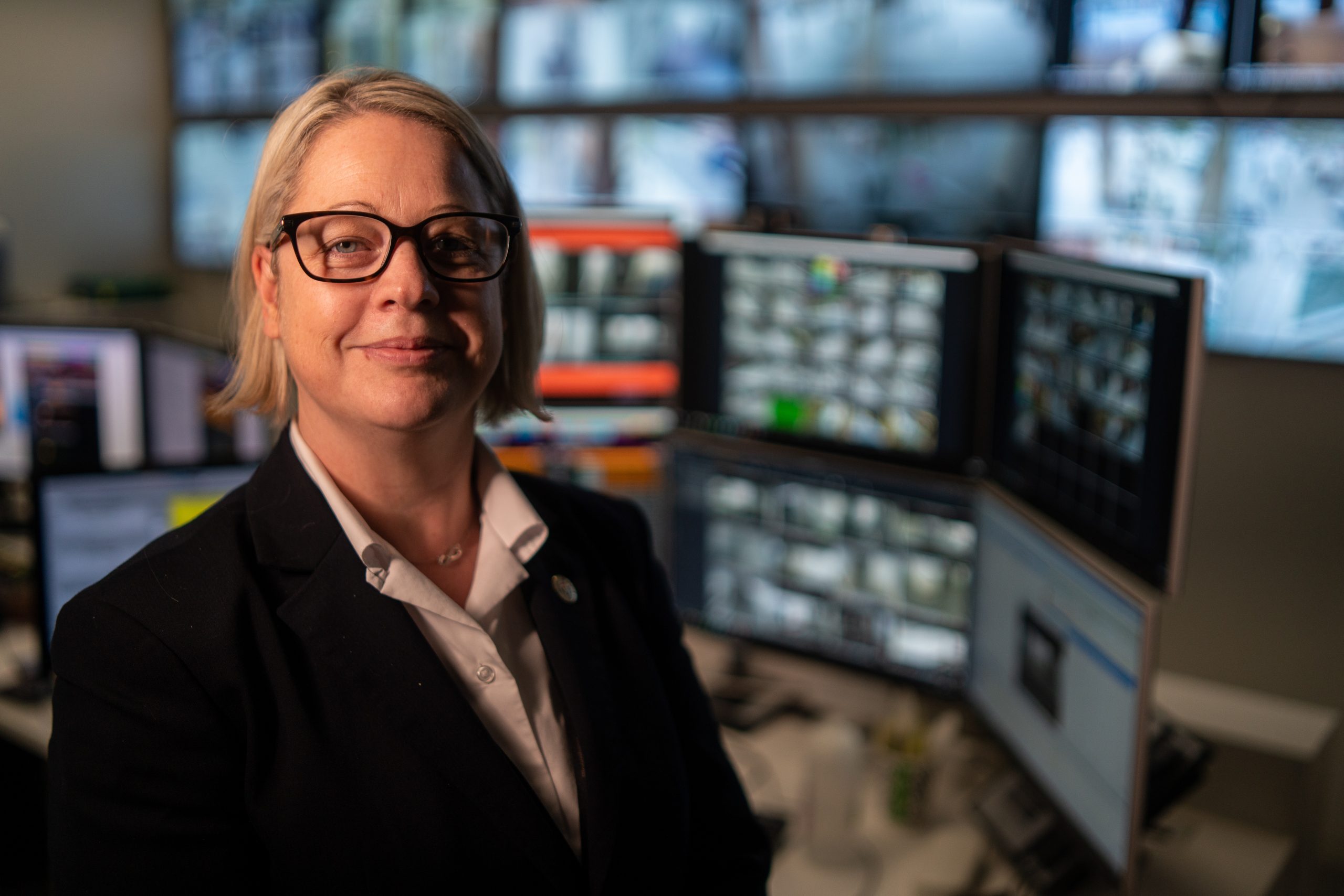 Business woman looks at the camera while computer screens turn on behind her