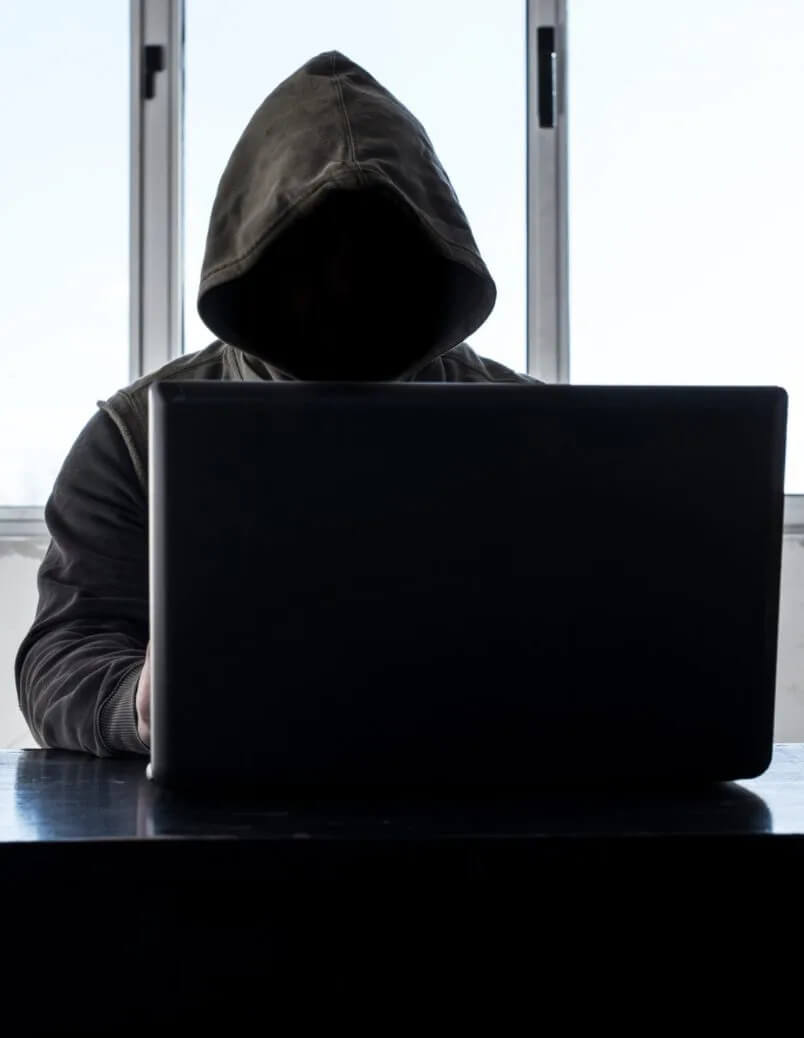 Man in hoodie covering his face working on a laptop
