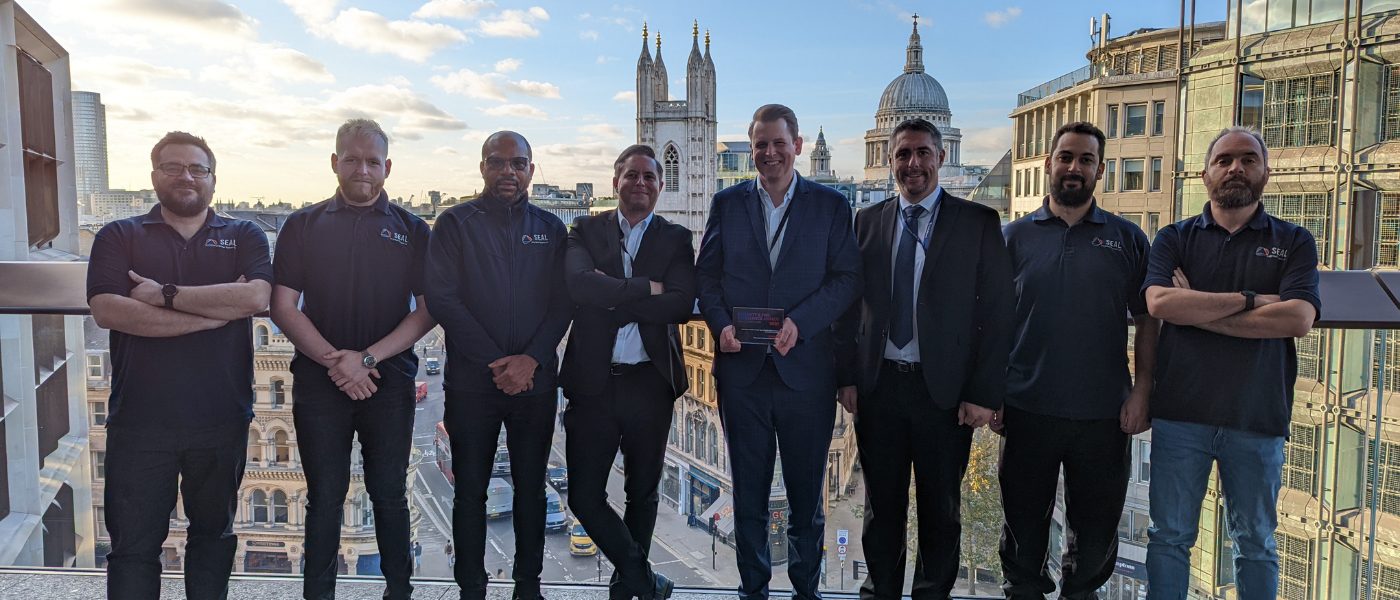 Group of eight men standing on a roof holding an award