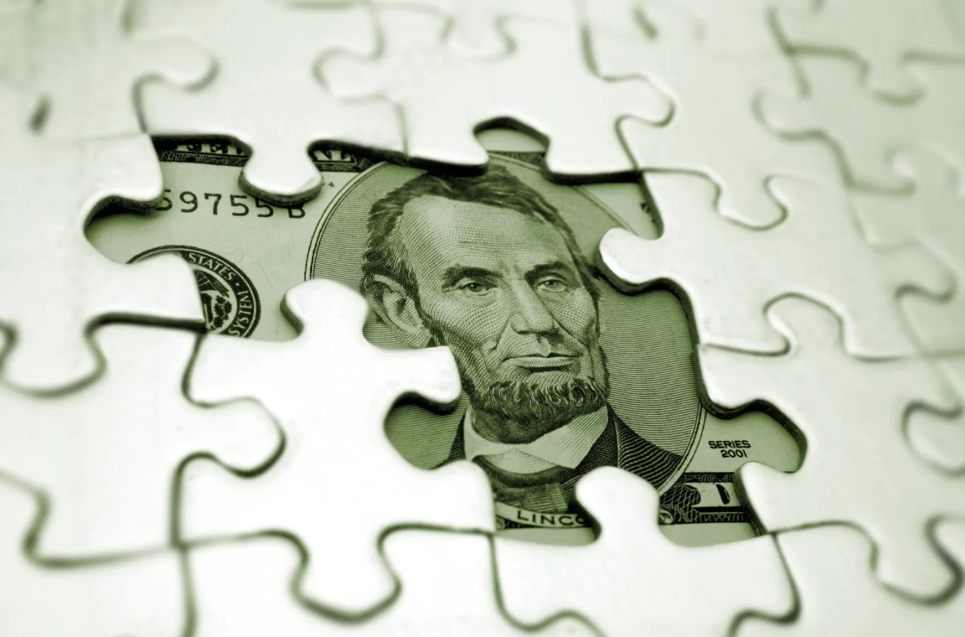 Lincoln's face on the five dollar bill shows from underneath an incomplete puzzle
