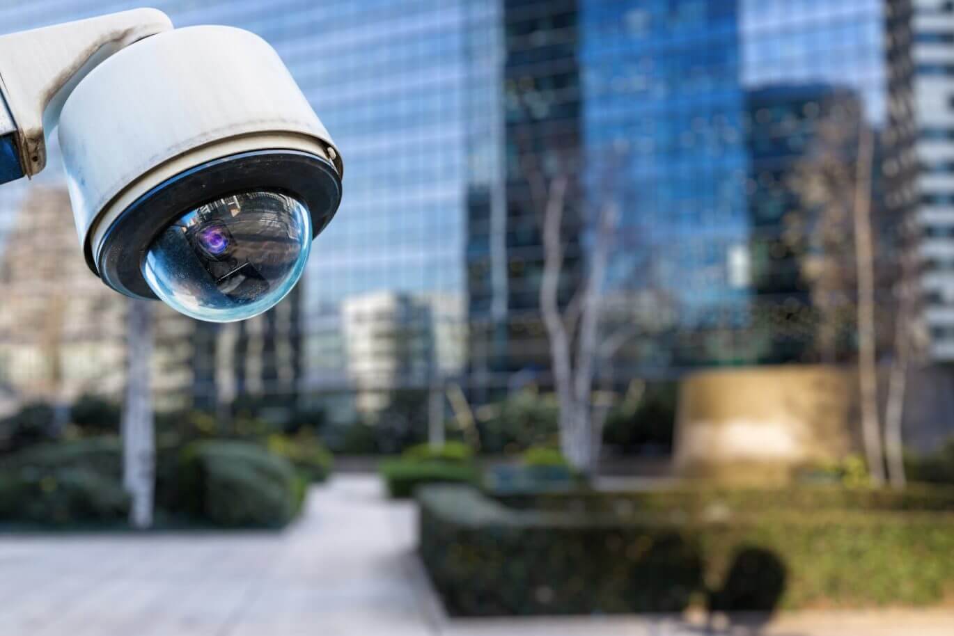 A round CCTV camera is in focus, while the blurred background shows a city location.