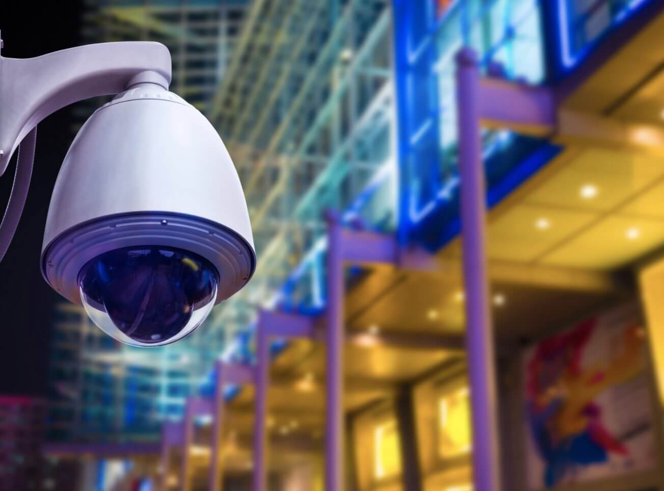 A CCTV security camera overlooks a sidewalk at night.