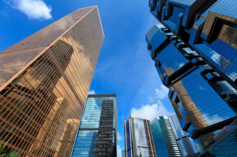 A view looking up at skyscrapers towards a blue sky with clouds.