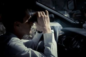 Man with binoculars looking out of a car windshield