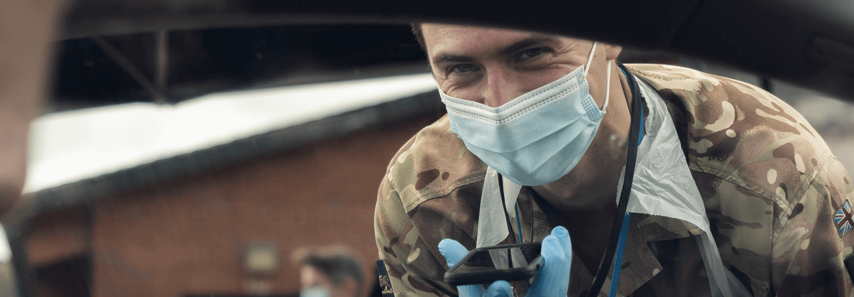 Soldier looking into a car window wearing a mask and holding a phone